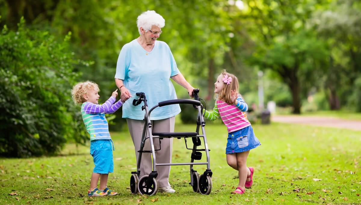 Grandmother with walker smiling at grand children enjoying a walk in the park