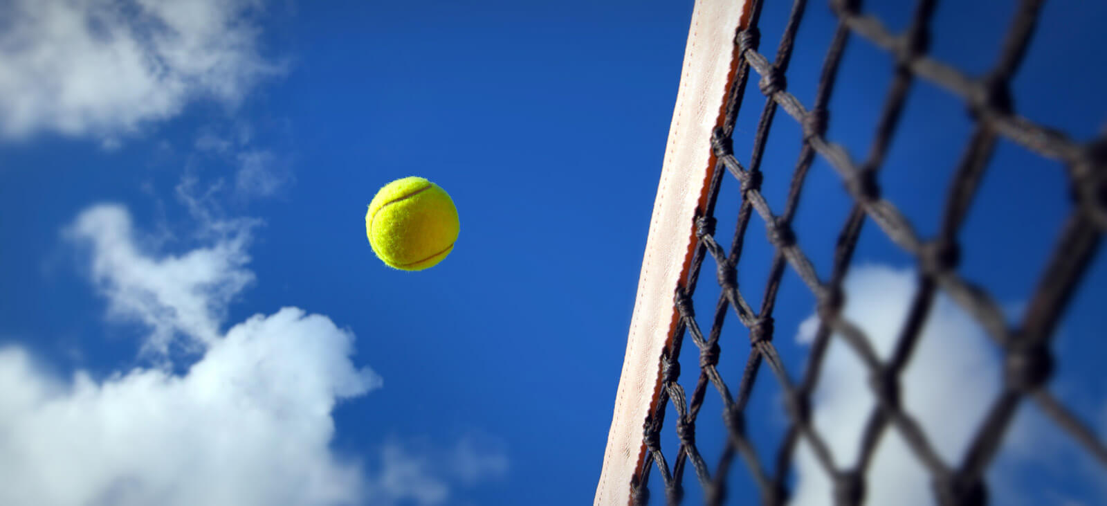 Tennis ball going over the net aginst blue sky