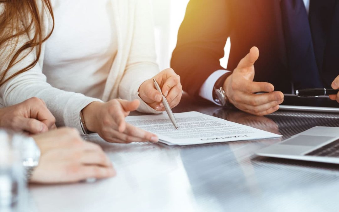 Business people discussing contract while working together in sunny modern office. Unknown businessman and woman with colleagues or lawyers at meeting.